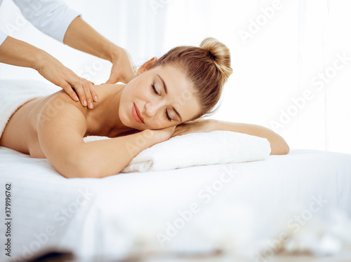 Young and blonde woman enjoying massage of back in spa salon. Beauty concept
