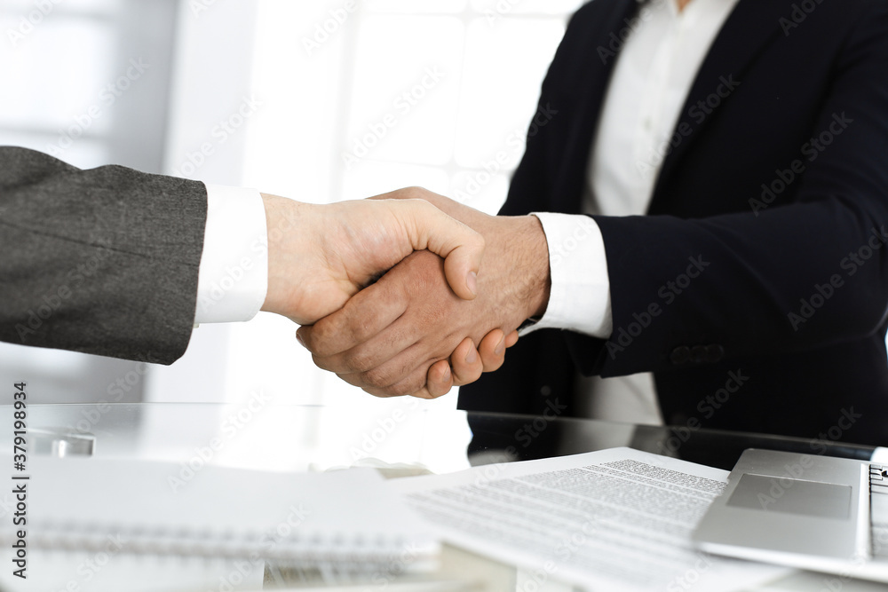 Unknown diverse business people are shaking hands finishing up meeting at the desk in office, close-up. Handshake concept Unknown diverse business people are shaking hands finishing up meeting at the desk in office, close-up. Handshake concept
