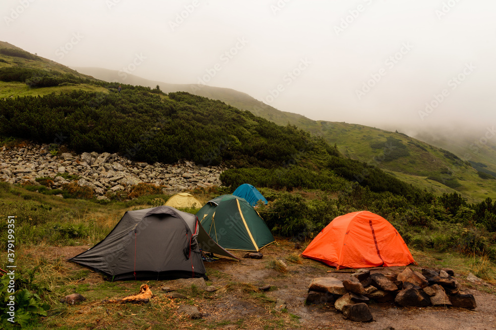 A small tent town in the mountains, tents by the lake in the mountains, the area near the lake Brebeneskul, the Carpathian mountains, fog and rain in the mountains.
