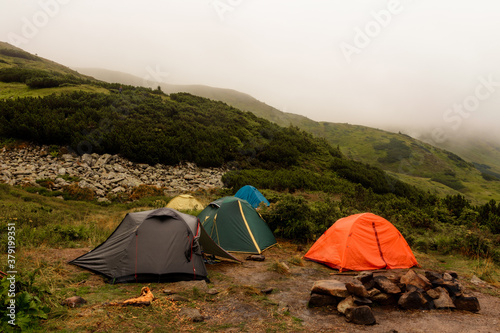 A small tent town in the mountains, tents by the lake in the mountains, the area near the lake Brebeneskul, the Carpathian mountains, fog and rain in the mountains.