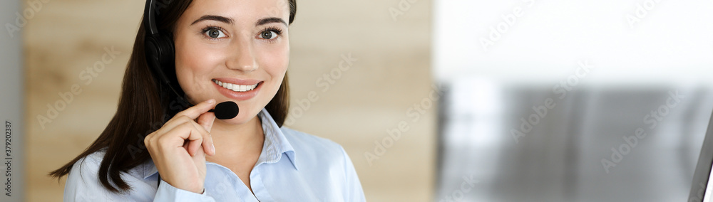 Brunette female customer service representative in a headset is consulting clients online. Call center and business people concept Brunette female customer service representative in a headset is consulting clients online. Call center and business people concept