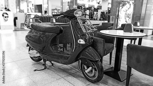 Black and white photo on the background of a shopping center. Classic scooter on the background of an empty cafe. Vintage background. Vintage style.