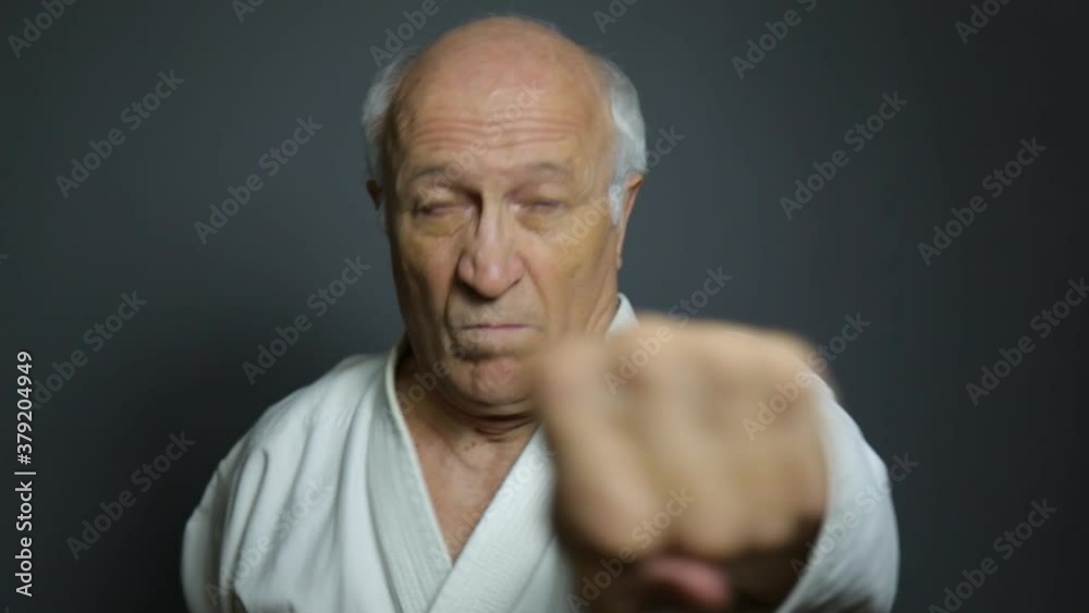 Old man athlete doing punches with hands on gray background Old man athlete doing punches with hands on gray background