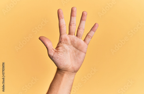 Arm and hand of caucasian man over yellow isolated background counting number 5 showing five fingers