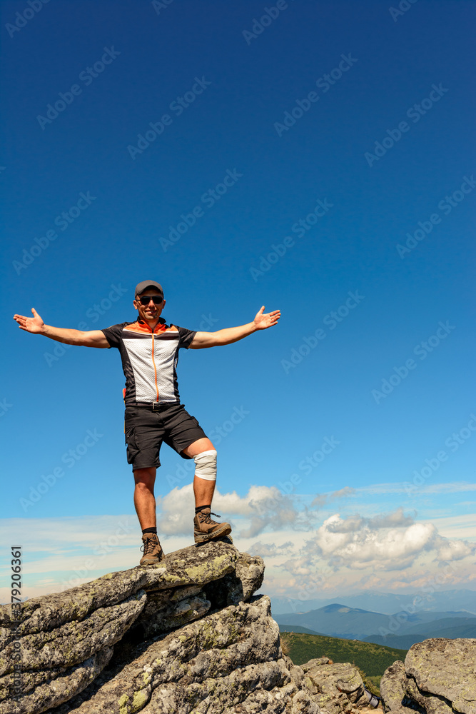 traveler, tourist, traveler stands on top of a cliff and enjoys a sunny day and a view of the picturesque Carpathians.