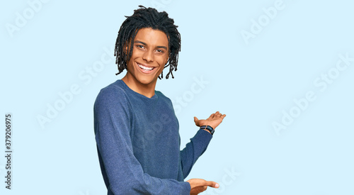 Young african american man wearing casual winter sweater inviting to enter smiling natural with open hand