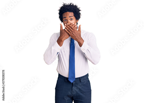 Handsome african american man with afro hair wearing business clothes shocked covering mouth with hands for mistake. secret concept.