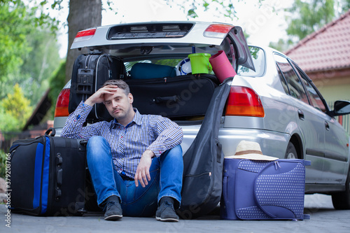 Φωτογραφία Handsome man sitting on the road next to car with open trunk