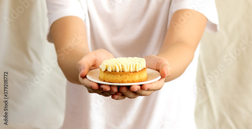 Selective focus to a child holding in hands a plate with vanilla cake.