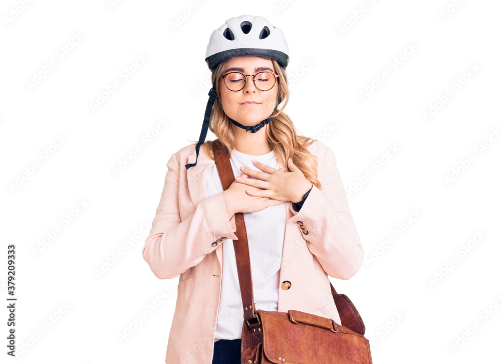 Young caucasian woman wearing bike helmet and leather bag smiling with hands on chest with closed eyes and grateful gesture on face. health concept. Young caucasian woman wearing bike helmet and leather bag smiling with hands on chest with closed eyes and grateful gesture on face. health concept.