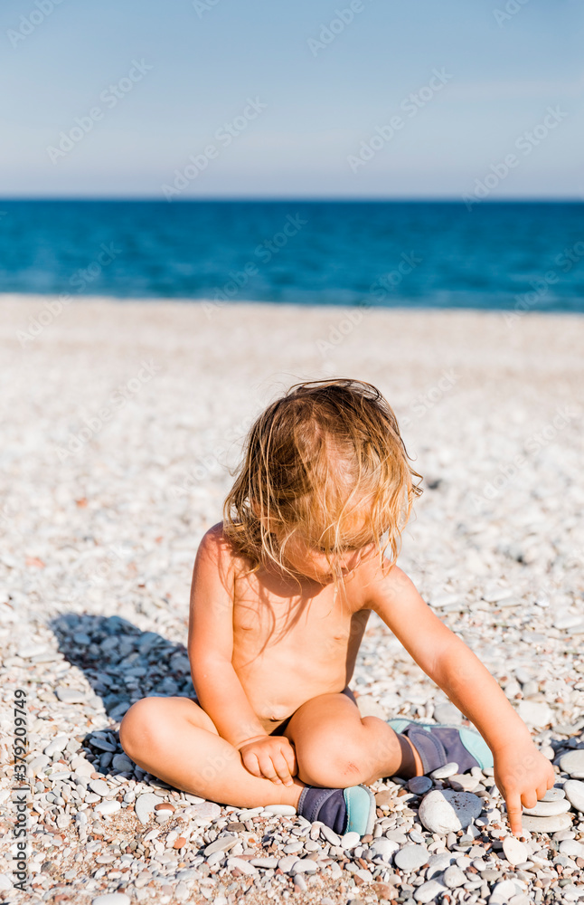 Toddler girl playing with pebbles on beach Toddler girl playing with pebbles on beach