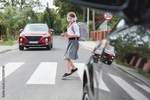 Scared girl with phone and headphones runs away from the car at a pedestrian crossing © Photographee.eu