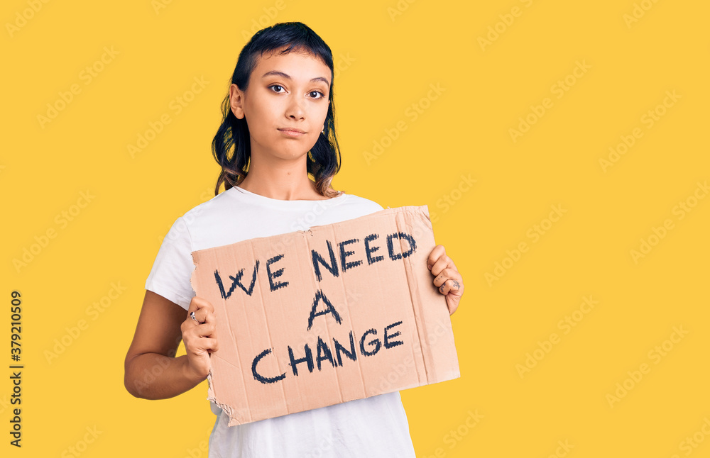 Young woman holding we need a change banner thinking attitude and sober expression looking self confident Young woman holding we need a change banner thinking attitude and sober expression looking self confident