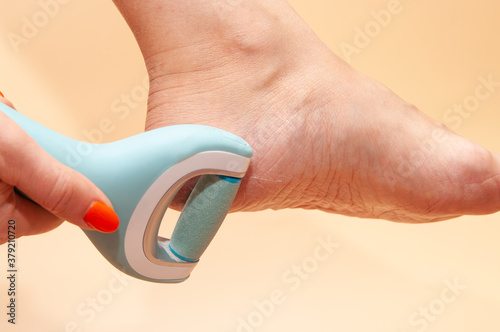 Care and cleansing of the woman feet from rough, flaky skin. An electric foot dead skin remover in a woman's hand grinds foot heel at home.