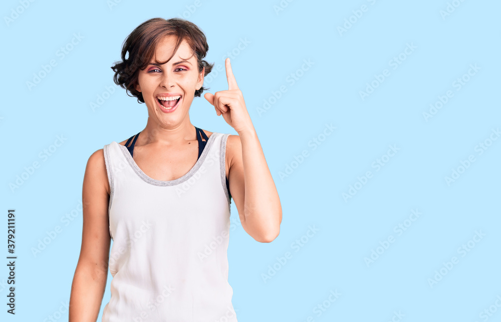 Beautiful young woman with short hair wearing casual sport clothes pointing finger up with successful idea. exited and happy. number one. Beautiful young woman with short hair wearing casual sport clothes pointing finger up with successful idea. exited and happy. number one.