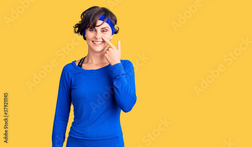 Beautiful young woman with short hair wearing training workout clothes pointing with hand finger to face and nose, smiling cheerful. beauty concept