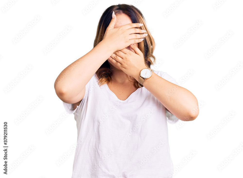 Young beautiful caucasian woman wearing casual white tshirt covering eyes and mouth with hands, surprised and shocked. hiding emotion Young beautiful caucasian woman wearing casual white tshirt covering eyes and mouth with hands, surprised and shocked. hiding emotion