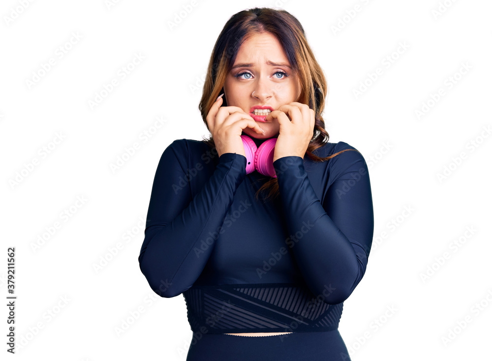 Young beautiful caucasian woman wearing gym clothes and using headphones looking stressed and nervous with hands on mouth biting nails. anxiety problem. Young beautiful caucasian woman wearing gym clothes and using headphones looking stressed and nervous with hands on mouth biting nails. anxiety problem.