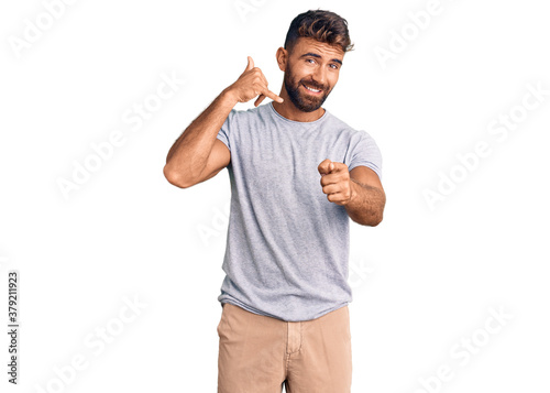 Young hispanic man wearing casual clothes smiling doing talking on the telephone gesture and pointing to you. call me.