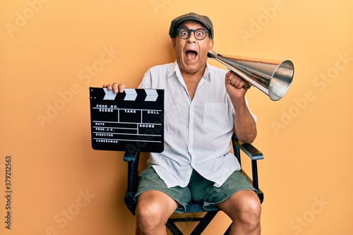 Handsome mature director man holding video film clapboard and louder celebrating crazy and amazed for success with open eyes screaming excited. photo