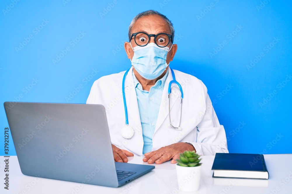 Senior handsome man with gray hair wearing doctor uniform and medical mask scared and amazed with open mouth for surprise, disbelief face Senior handsome man with gray hair wearing doctor uniform and medical mask scared and amazed with open mouth for surprise, disbelief face