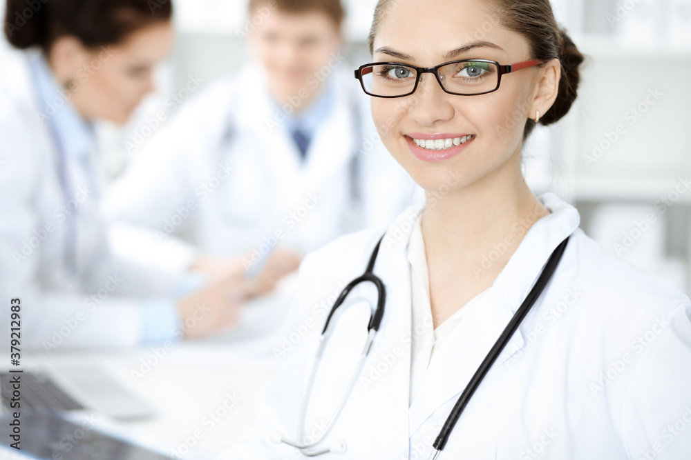 Happy smiling woman-doctor sitting and looking at camera at meeting with medical staff . Medicine concept Happy smiling woman-doctor sitting and looking at camera at meeting with medical staff . Medicine concept
