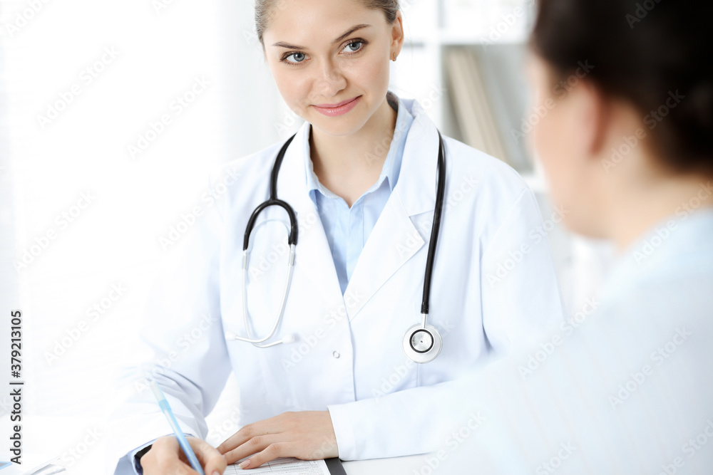 Friendly smiling doctor and patient sitting at the table. Very good news and high level medical service concept Friendly smiling doctor and patient sitting at the table. Very good news and high level medical service concept