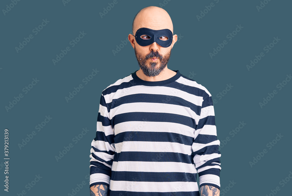 Obraz premium Young handsome man wearing burglar mask making fish face with lips, crazy and comical gesture. funny expression.