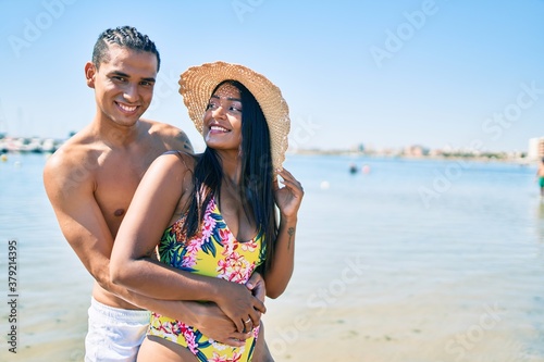 Young latin couple wearing swimwear smiling happy and hugging at the beach.