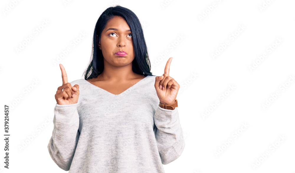 Hispanic woman with long hair wearing casual clothes pointing up looking sad and upset, indicating direction with fingers, unhappy and depressed. Hispanic woman with long hair wearing casual clothes pointing up looking sad and upset, indicating direction with fingers, unhappy and depressed.