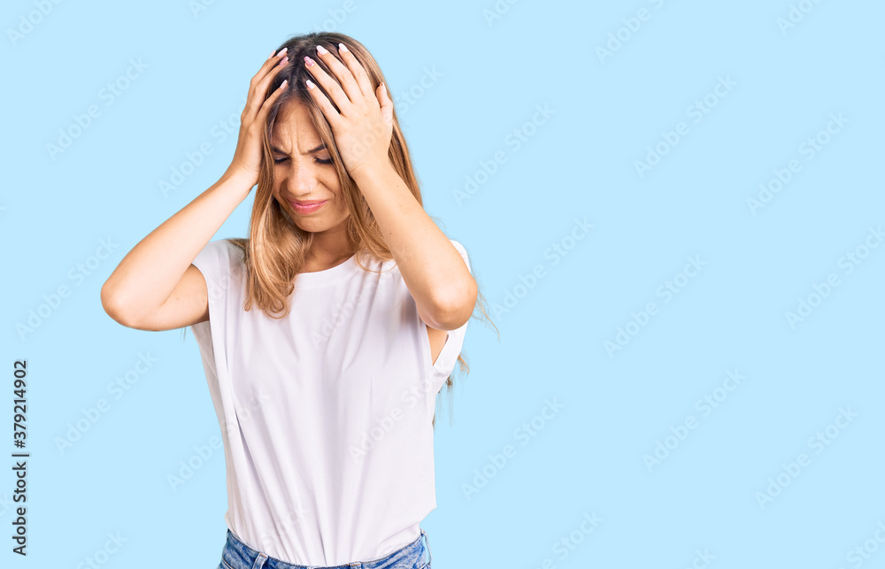 Fototapeta premium Beautiful caucasian woman with blonde hair wearing casual white tshirt suffering from headache desperate and stressed because pain and migraine. hands on head.