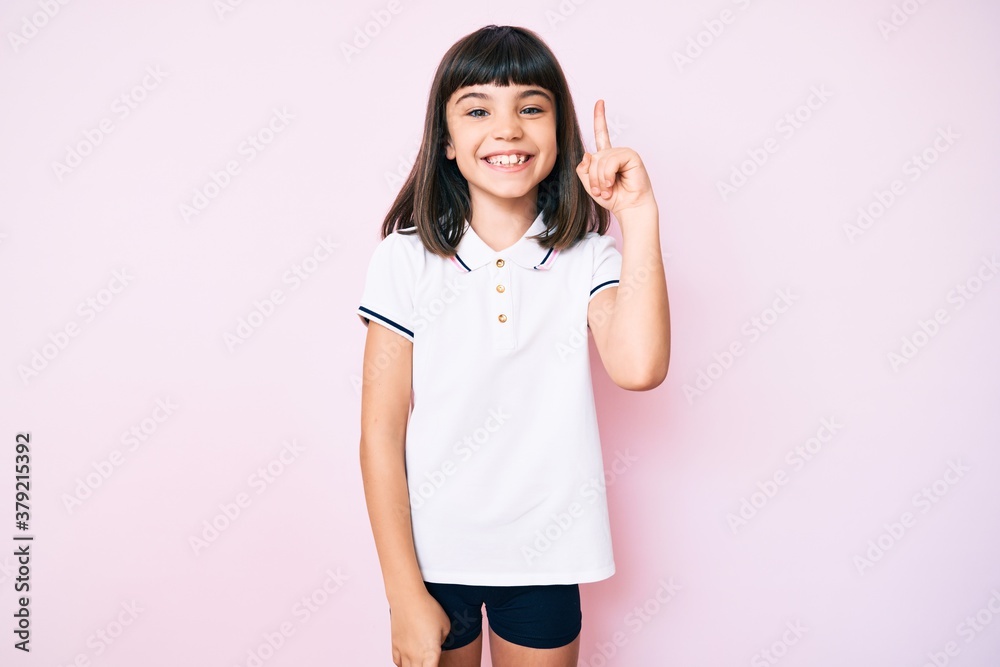 Young little girl with bang wearing sportswear pointing finger up with successful idea. exited and happy. number one.