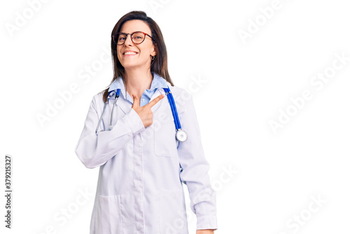 Young beautiful woman wearing doctor stethoscope and glasses cheerful with a smile of face pointing with hand and finger up to the side with happy and natural expression on face