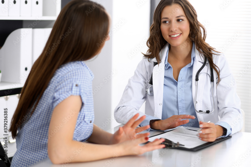 Doctor and happy patient talking while sitting at the desk. The physician or therapist discussing healthy lifestyle. Health care, medicine and patient service concept Doctor and happy patient talking while sitting at the desk. The physician or therapist discussing healthy lifestyle. Health care, medicine and patient service concept