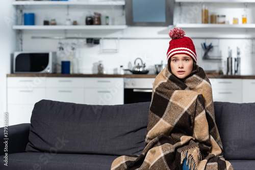 Konstfotografi freezing woman in knitted hat, covering with warm plaid blanket while sitting on