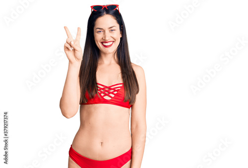 Young beautiful caucasian woman wearing bikini showing and pointing up with fingers number two while smiling confident and happy. photo