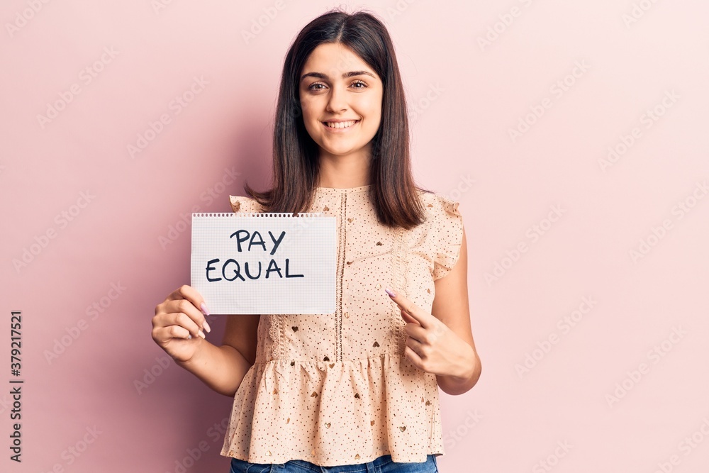 Young beautiful girl holding pay equal paper smiling happy pointing with hand and finger Young beautiful girl holding pay equal paper smiling happy pointing with hand and finger