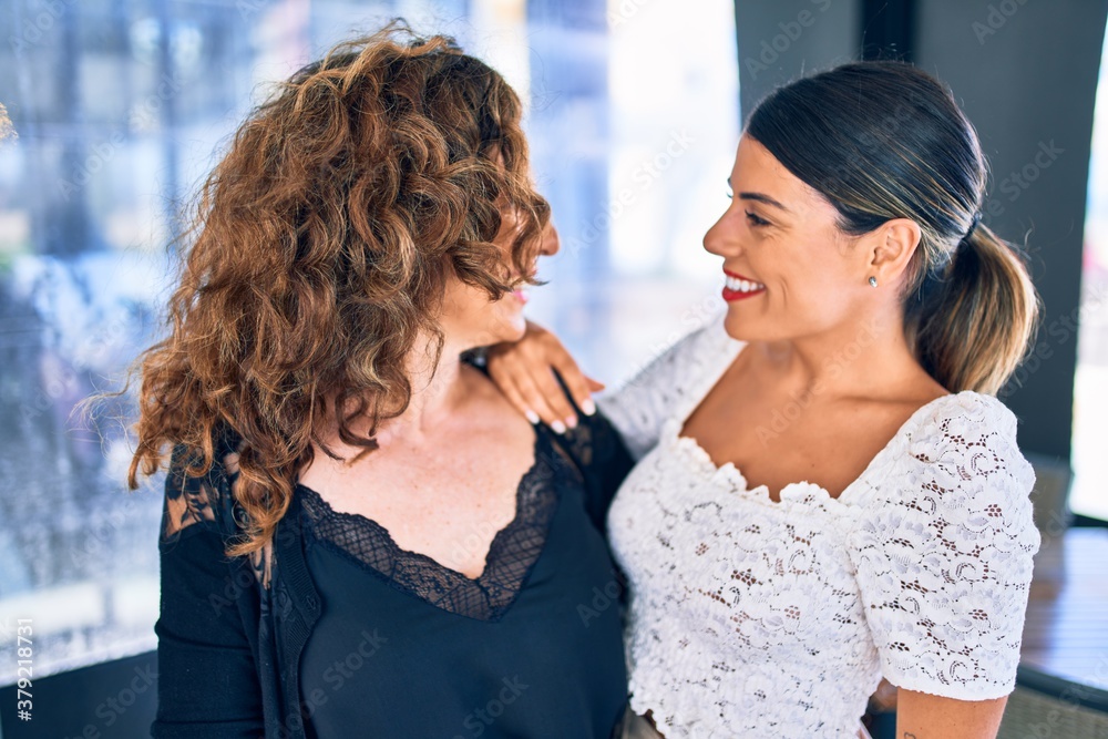 Naklejka premium Beautiful mother and daughter smiling happy and confident. Standing with smile on face hugging at restaurant