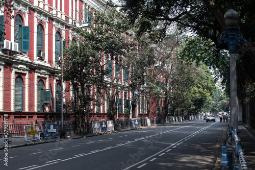 Kolkata, India - February 1, 2020: Three unidentified people walks on the street with two passing cars next to a red house facade on February 1, 2020 in Kolkata, India © Arvid Norberg