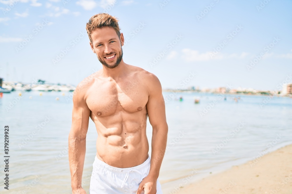 Handsome fitness caucasian man at the beach on a sunny day showing muscular fitness body Handsome fitness caucasian man at the beach on a sunny day showing muscular fitness body