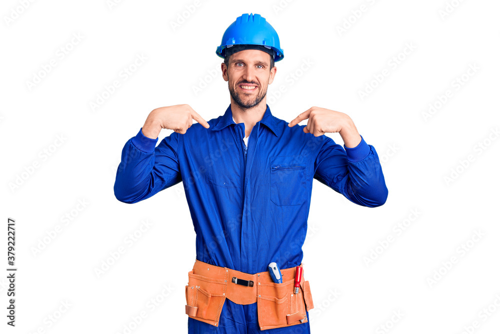 Young handsome man wearing worker uniform and hardhat looking confident with smile on face, pointing oneself with fingers proud and happy.