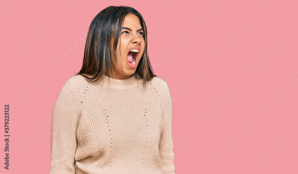 Young latin girl wearing wool winter sweater angry and mad screaming frustrated and furious, shouting with anger. rage and aggressive concept. Young latin girl wearing wool winter sweater angry and mad screaming frustrated and furious, shouting with anger. rage and aggressive concept.