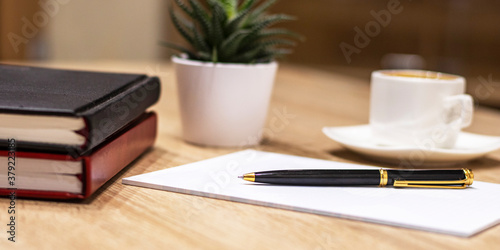 Side view of a pen with a red and black diary and a cup of coffee on a wooden table. Office workplace. Business concept.
