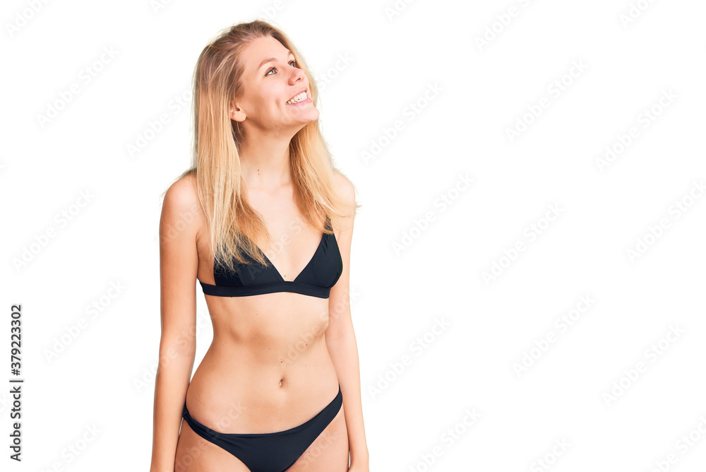 Young beautiful blonde woman wearing bikini looking away to side with smile on face, natural expression. laughing confident. Young beautiful blonde woman wearing bikini looking away to side with smile on face, natural expression. laughing confident.