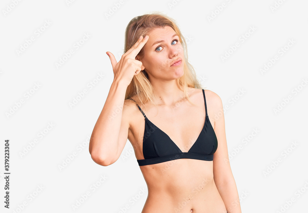 Fototapeta premium Young beautiful blonde woman wearing bikini shooting and killing oneself pointing hand and fingers to head like gun, suicide gesture.