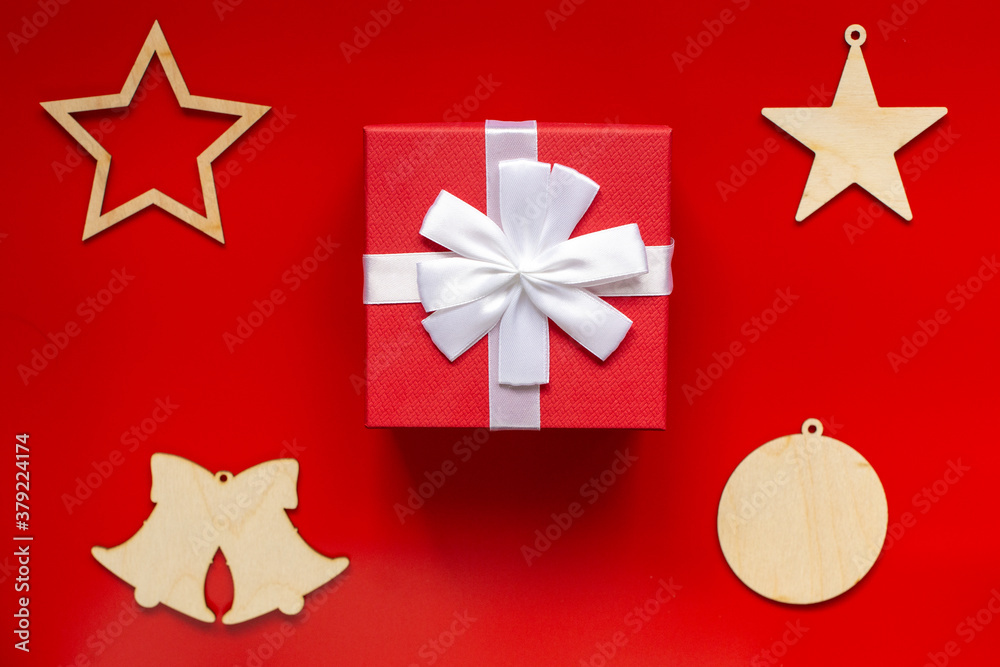 Red gift box with white bow and Christmas wooden decorations in the form of stars, bells and ball, on a red background