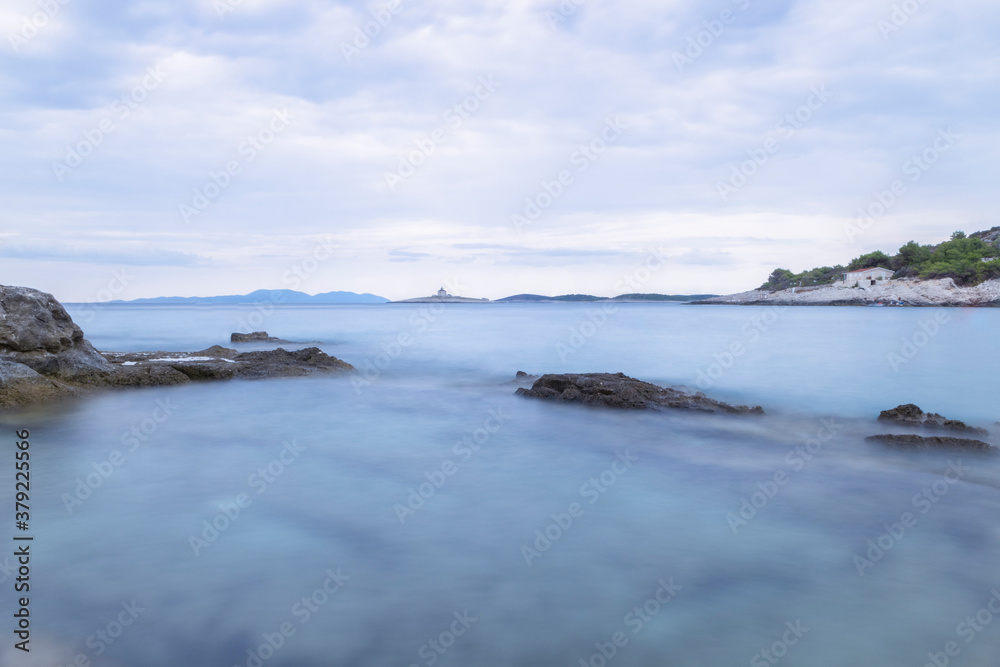 Obraz premium Long exposure photo of Pokonji Dol island with stone lighthouse in the distance, surrounded by silky, adriatic sea surface
