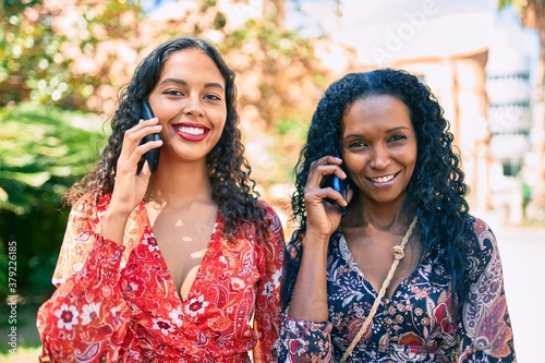 African american mother and daughter smiling happy talking on the smartphone at park,