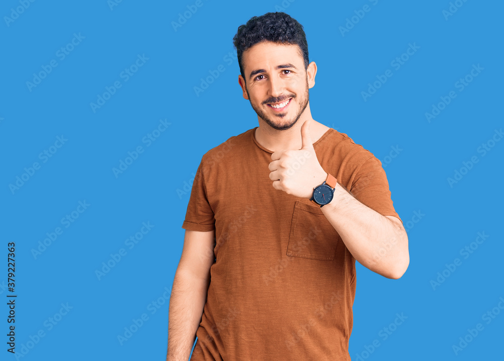 Young hispanic man wearing casual clothes doing happy thumbs up gesture with hand. approving expression looking at the camera showing success. Young hispanic man wearing casual clothes doing happy thumbs up gesture with hand. approving expression looking at the camera showing success.