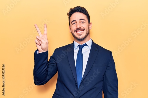 Young hispanic man wearing suit showing and pointing up with fingers number two while smiling confident and happy.